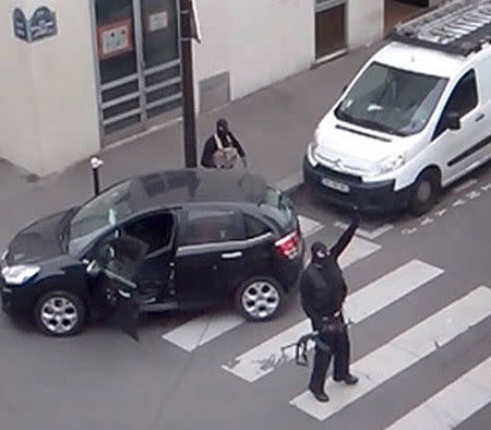 Gunmen gesture as they return to their car after the attack outside the offices of French satirical weekly newspaper Charlie Hebdo (seen at rear) in this still image taken from amateur video shot in Paris January 7, 2015. REUTERS/Reuters TV