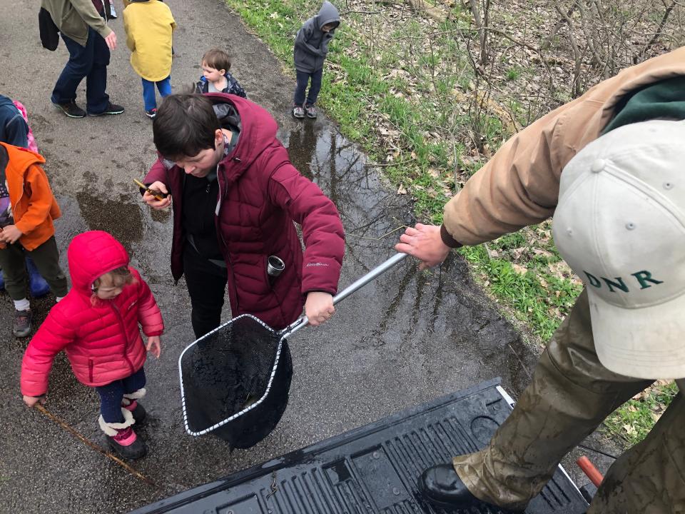 Indiana state biologist Tom Bacula hands a net with rainbow trout from his truck to Molly Emmons and her daughter, Raina Parkes, so they can help stock Potato Creek on April 28, 2022, at Potato Creek State Park in North Liberty.