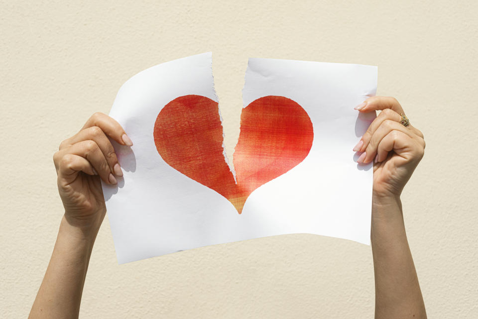 Hands tearing a paper with a heart, symbolizing a breakup or heartache