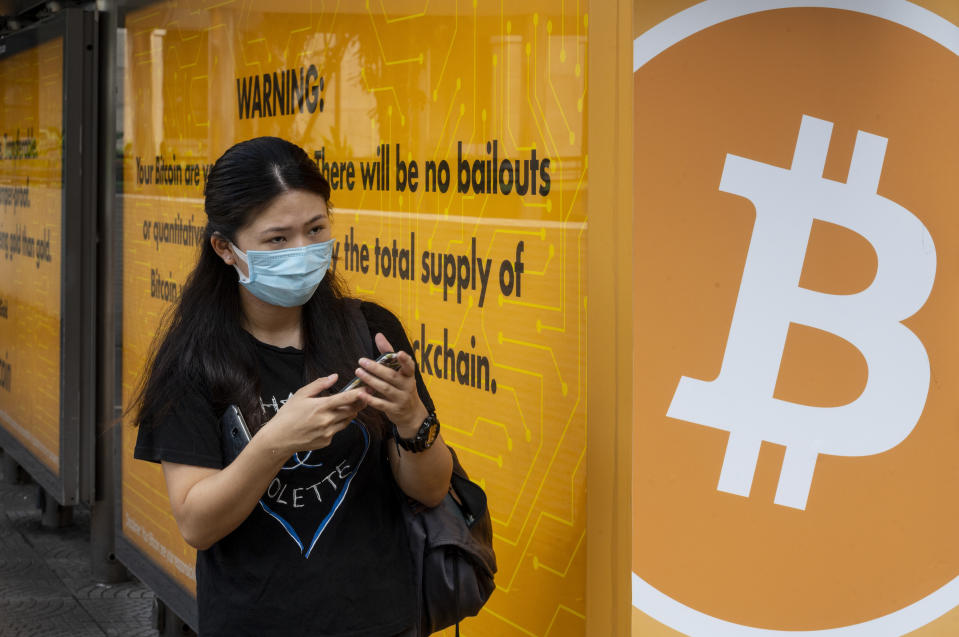 HONG KONG, CHINA - 2020/09/24: A woman wearing a mask stands next to a bus stop covered with Cryptocurrency electronic cash Bitcoin advertisement in Hong Kong. (Photo by Budrul Chukrut/SOPA Images/LightRocket via Getty Images)