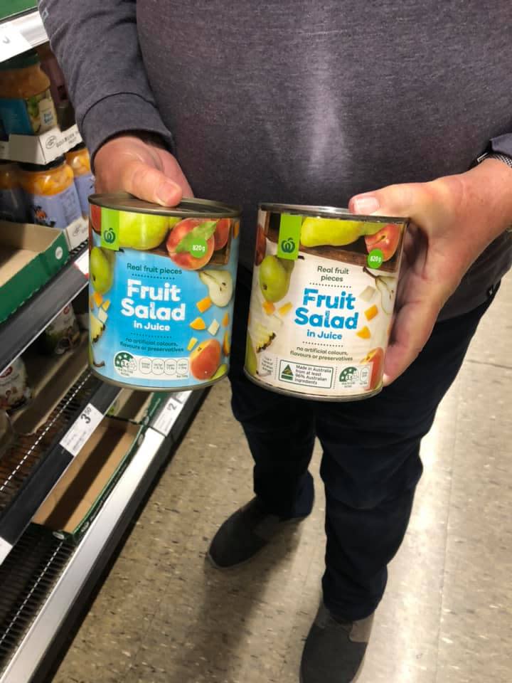 Person holding two Woolworths canned fruit salads.