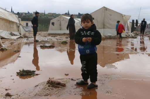 Displaced Syrians stand in puddles of water at the Deir al-Ballut refugee camp in Afrin's countryside, after heavy rains bring floods