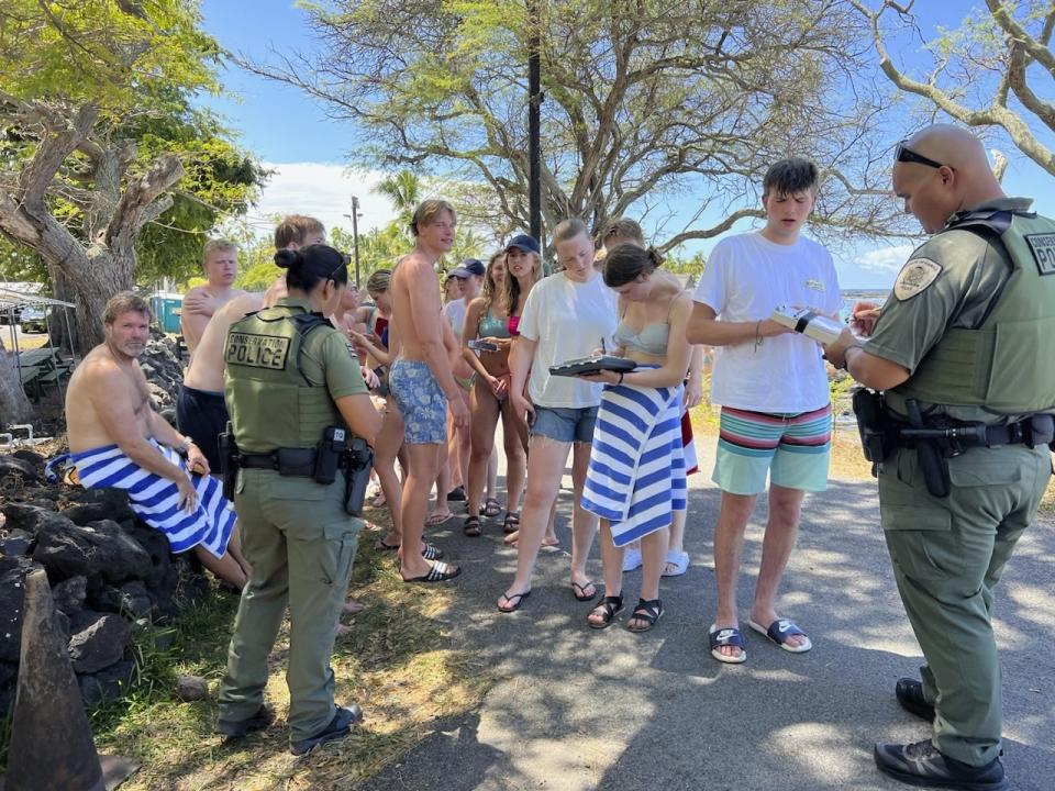 In this photo provided by the Hawaii Department of Land and Natural Resources, department enforcement officers speak to swimmers in Honaunau, Hawaii, March 26, 2023, after the swimmers allegedly harassed a pod of wild spinner dolphins. (Hawaii Department of Land and Natural Resources via AP)