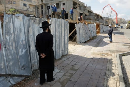 Ultra-orthodox Jews walk in the Israeli settlement of Beitar Illit as Palestinian labourers work at a construction site on February 14, 2018