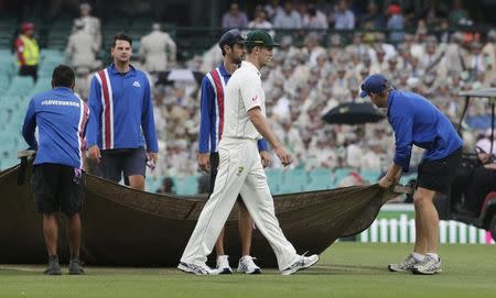 Australian cricket player Mitchell Marsh walks off the pitch as the covers are put on during a rain delay in their third cricket test against the West Indies at the SCG in Sydney, January 4, 2016. REUTERS/Jason Reed