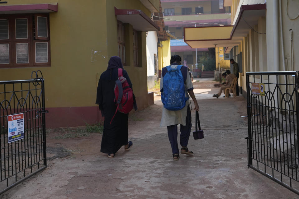 A girl in uniform walks into the government-run junior college with a Muslim student wearing burqa in Udupi, Karnataka state, India, Feb. 25, 2022. Muslim students in this southern Indian state have found themselves at the center of a debate over hijab bans in schools. The furor began in January when staffers at the college began refusing admission to girls who showed up in a hijab, saying they were violating the uniform code. (AP Photo/Aijaz Rahi)