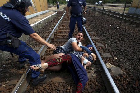 Hungarian policemen stand over a family of immigrants who threw themselves onto the track before they were detained at a railway station in the town of Bicske, Hungary, September 3, 2015. REUTERS/Laszlo Balogh