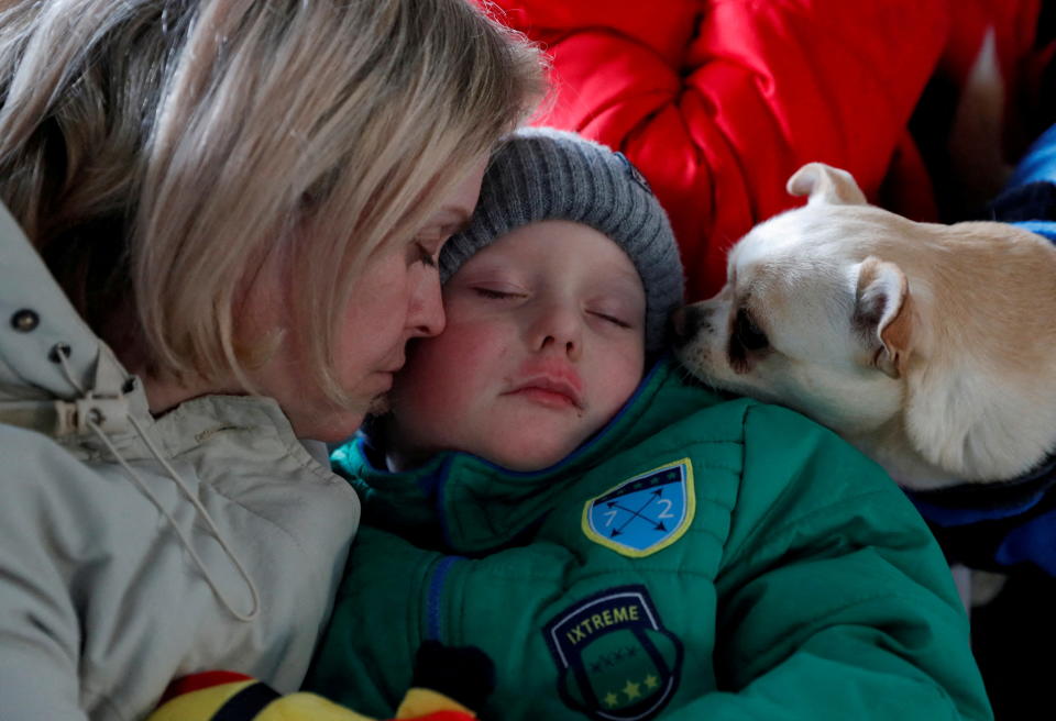 A woman comforts her child as a dog looks on. 