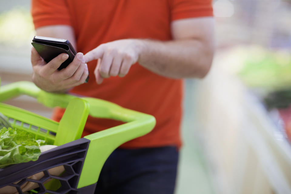 A man using his phone next to his grocery cart