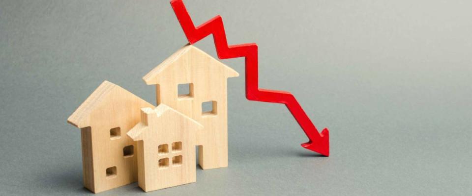 Miniature wooden houses and a red arrow down. The concept of falling mortgage rates.