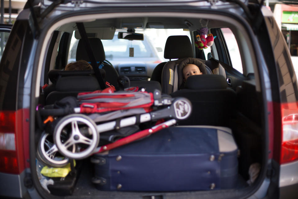 diaper bag and stroller in trunk of car with baby peering over seat