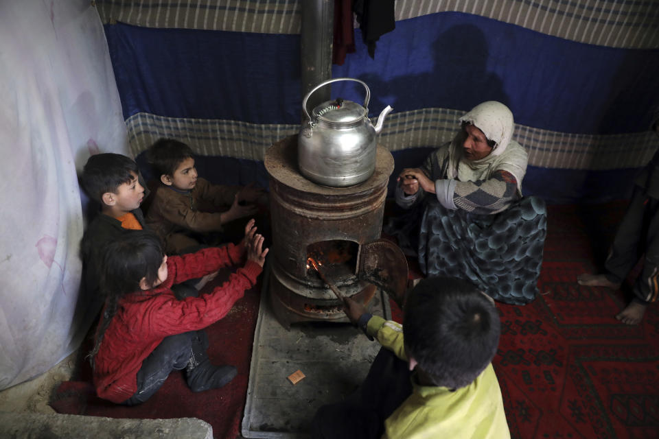 Internally displaced children sit around a stove to keep warm in a temporary shelter in the city of Kabul, Afghanistan, Wednesday, Dec. 30, 2020. Save the Children has warned that more than 300,000 Afghan children face freezing winter conditions that could lead to illness, in the worst cases death, without proper winter clothing and heating. (AP Photo/Rahmat Gul)