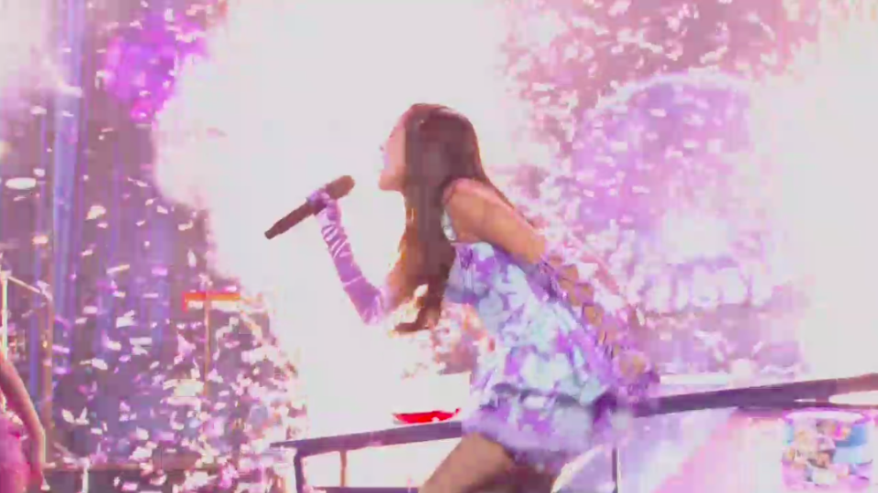 Olivia singing intensely and surrounded by glitter