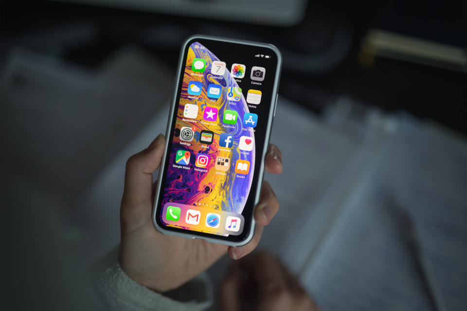 Celje, Slovenia - October 07, 2018: Woman holding new iPhone XS smartphone (with protective VRS design case, 5.8 inch Retina display, silver color version with 256 GB memory) in her hand over the note pad.