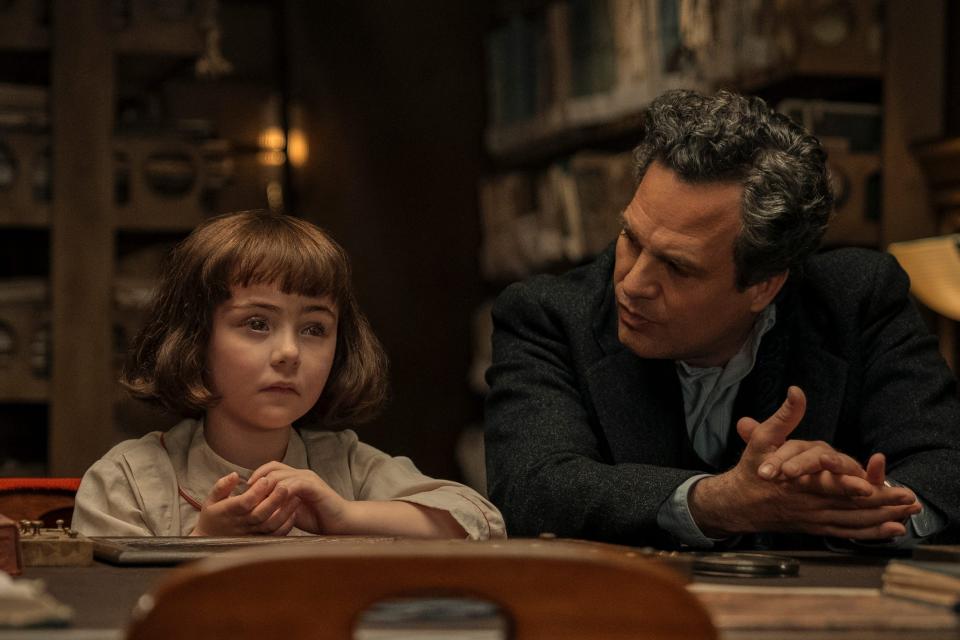 nell sutton as young marie-laure, sitting next to mark ruffalo playing her father. marie-laure is a young girl with a bob cut, and she's looking into the distance while her father gazes at her