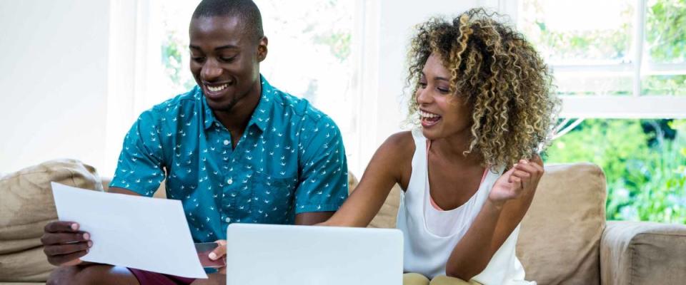 Happy couple checking bills while using laptop in living room