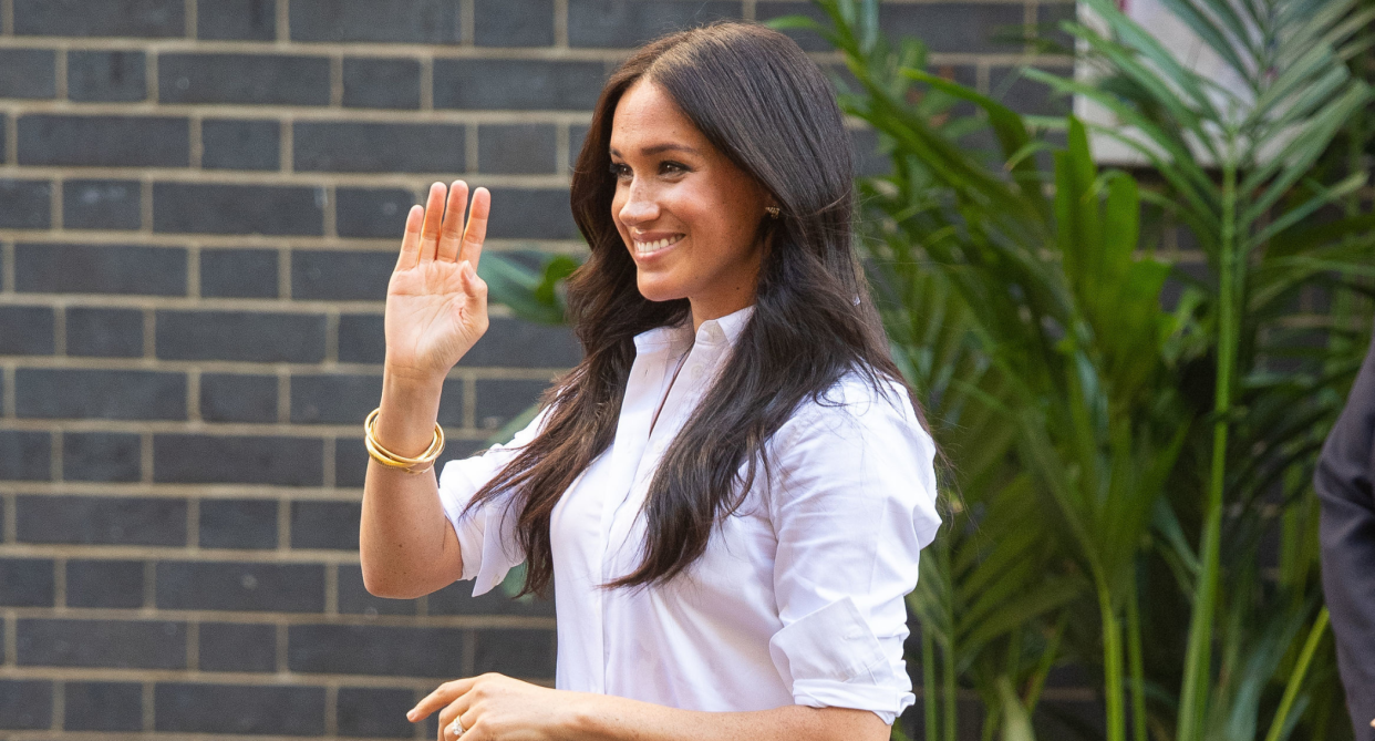 meghan markle smiling and waving wearing white button-down shirt and gold bracelet