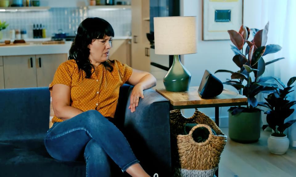 Still from an Amazon promo video. A woman sits on a couch in a posh home, looking at an Echo speaker on her end table with a concerned look on her face.