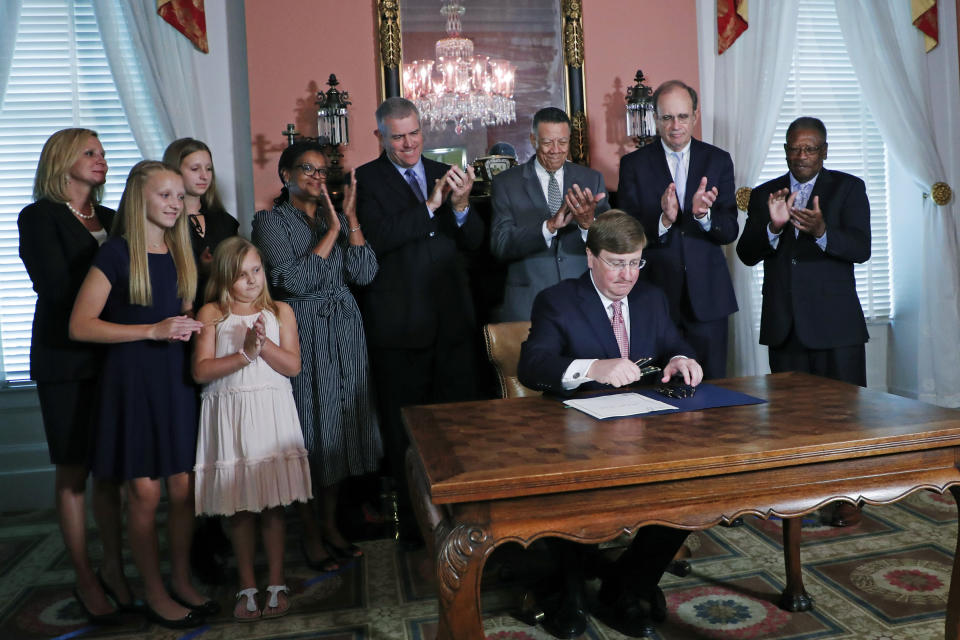 Mississippi Republican Gov. Tate Reeves signs the bill retiring the last state flag in the United States with the Confederate battle emblem, at the Governor's Mansion in Jackson, Miss., Tuesday, June 30, 2020. Family members are at left. Applauding are, from fifth from left, Sen. Angela Turner Ford, D-West Point; House Speaker Philip Gunn, R-Clinton; Reuben Anderson, former Mississippi Supreme Court Justice; Lt. Gov. Delbert Hosemann; and Transportation Commissioner for the Central District Willie Simmons. (AP Photo/Rogelio V. Solis, Pool)