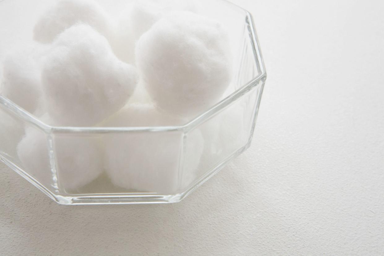 A glass bowl filled with cotton balls against a white background