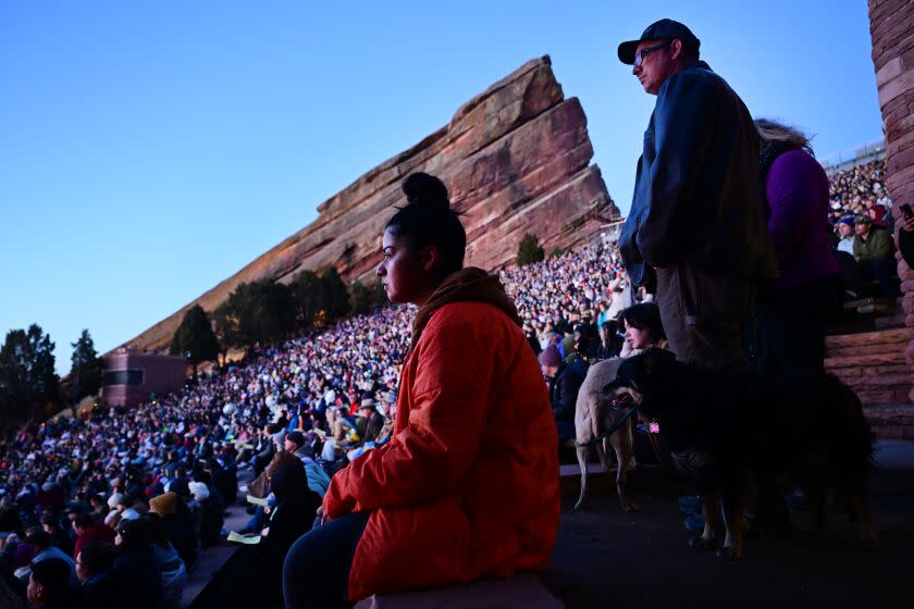 Concertgoer dressed in red jacket sitting along the edge of an amphitheater packed with other attendees