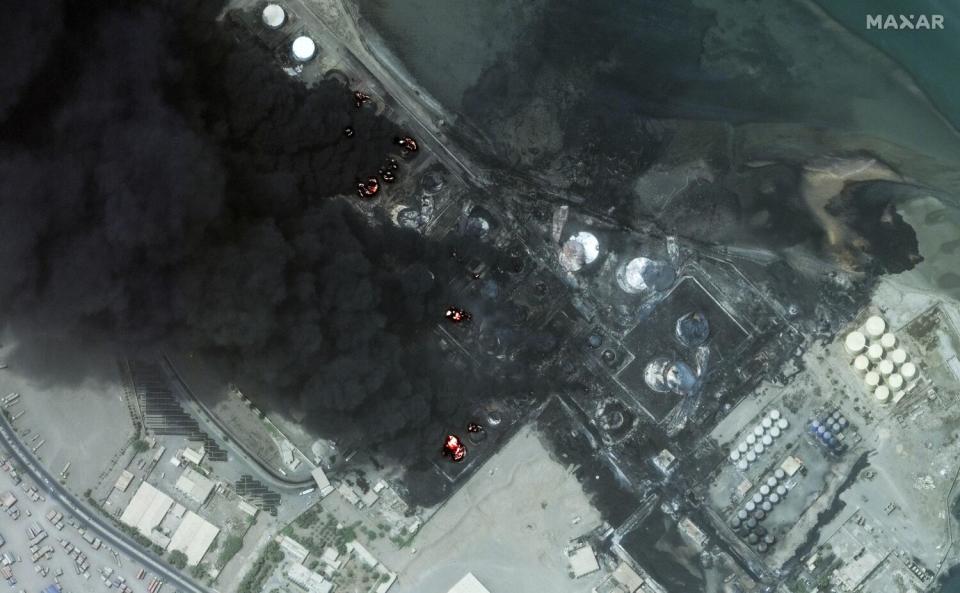 A satellite image shows smoke rising from burning oil tanks.