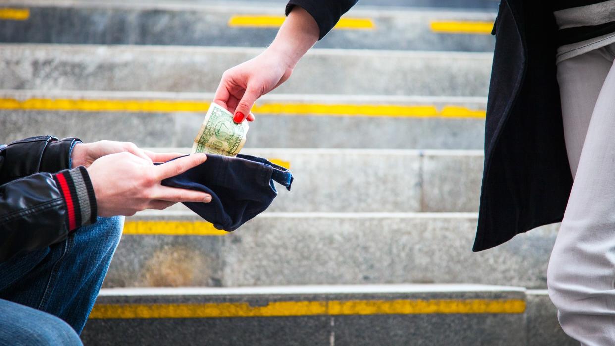 Woman giving money to homeless person in an urban passageway.