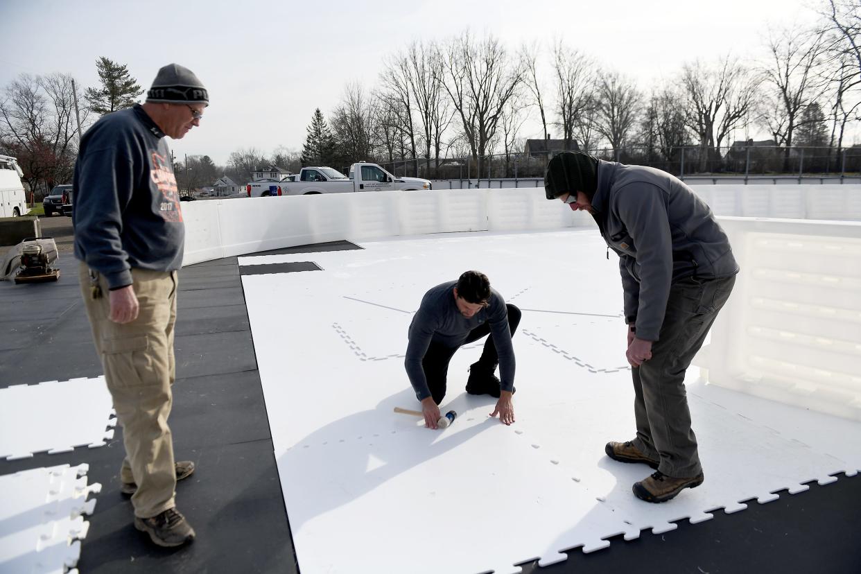 Massillon Parks and Recreation Department Superintendent Joe Pape, left, and maintenance supervisor Chris Moser, right, with the help of Chris Crowley with Global Synthetic Ice, build a skating rink in Wampler Park. The rink opens Tuesday.