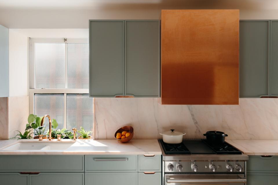 A copper-cladding hood creates an elegant pop of color in this pale blue kitchen designed by Home Studios.