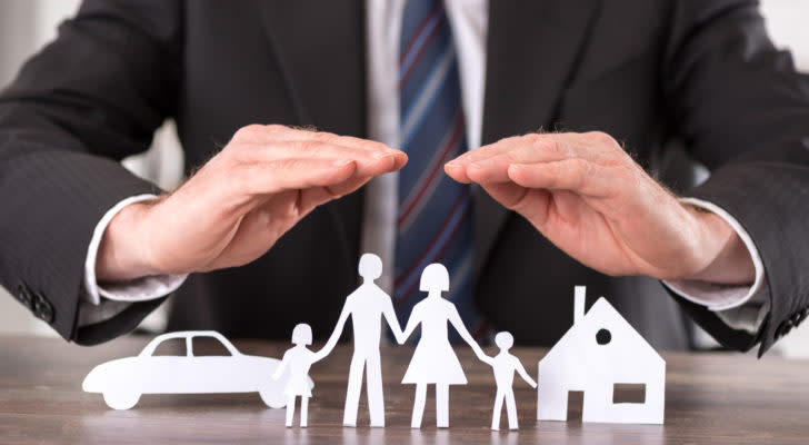 Man in suit with hands over paper cutouts of family, car and home. Represents insurance.