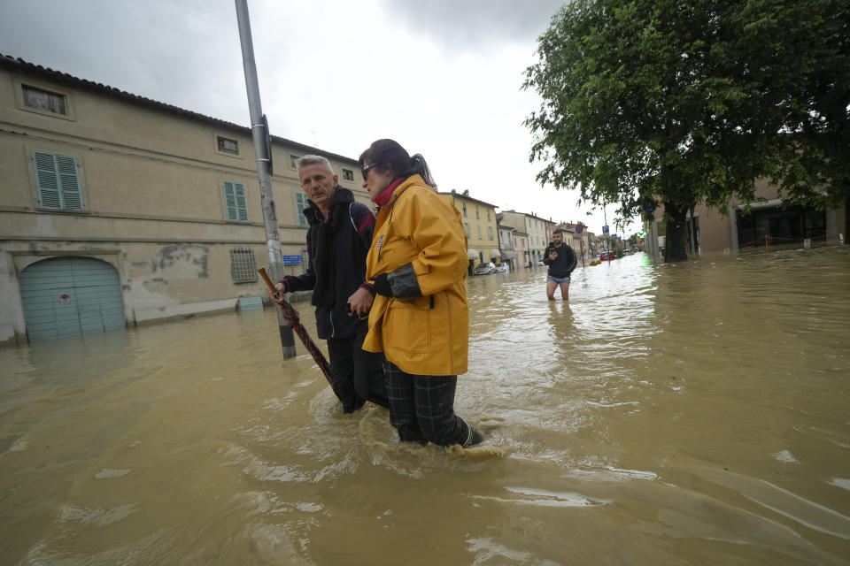 A couple makes its way through a flooded street in the village of Castel Bolognese, Italy, Wednesday, May 17, 2023. Exceptional rains Wednesday in a drought-struck region of northern Italy swelled rivers over their banks, killing at least eight people, forcing the evacuation of thousands and prompting officials to warn that Italy needs a national plan to combat climate change-induced flooding. (AP Photo/Luca Bruno)