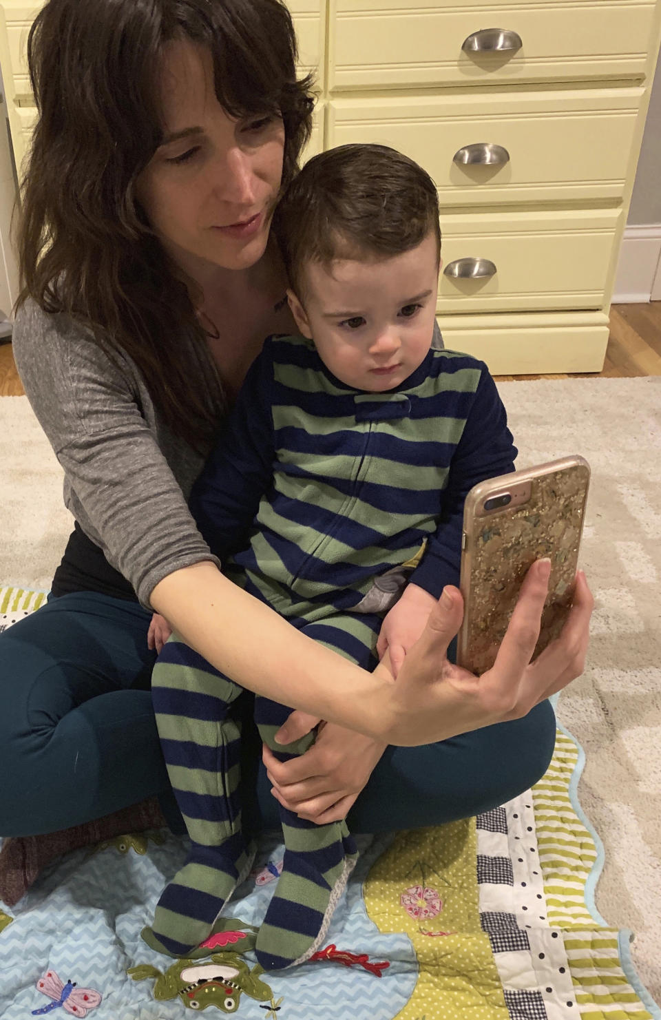 This March 30, 2020, photo taken on a self timer provided by Melissa Biddle shows herself with her 20-month-old son as they talk on the phone with the boy's father in Delaware County, Pa. The coronavirus is wreaking havoc on divorced families' custody arrangements as parents get sick or exposed to the illness. Biddle said she's caring full-time for her son because her ex-husband has been working to repair heating and air systems in grocery stores, and they both agreed this carried too much risk. (Melissa Biddle via AP)