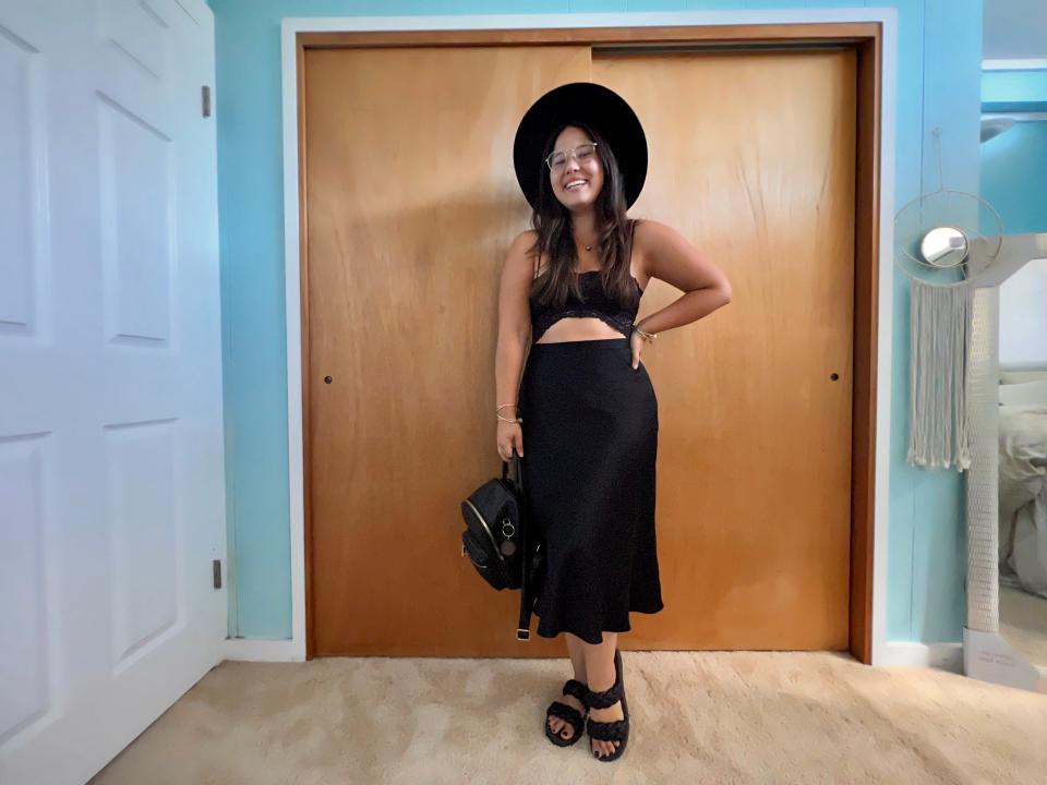 Author posing with black sandals, black dress, black wide-brimmed hat, and black bag.