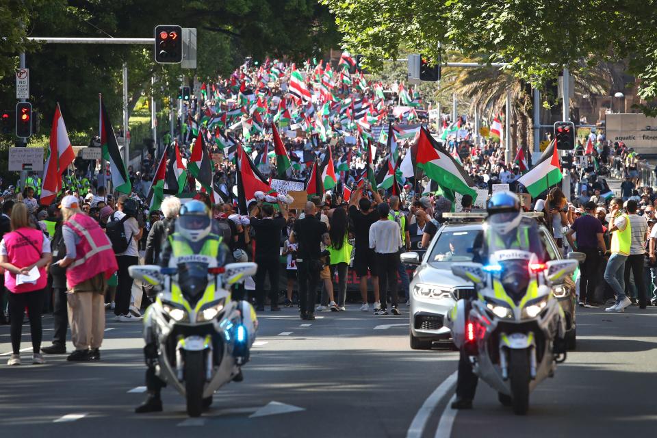 Protesters holding Palestinian flags march on a street in Sydney, Australia.