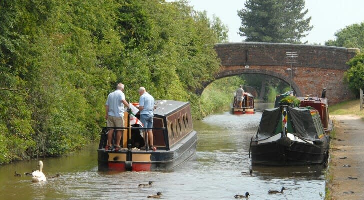 Two elderly men on a small barge traveling down a canal in Britain.