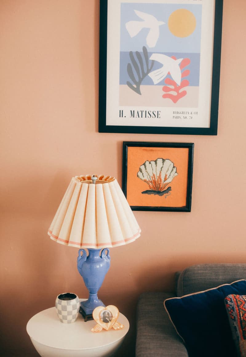 Blue lamp with light peach shade sits on accent table under art in living room with peach wall.
