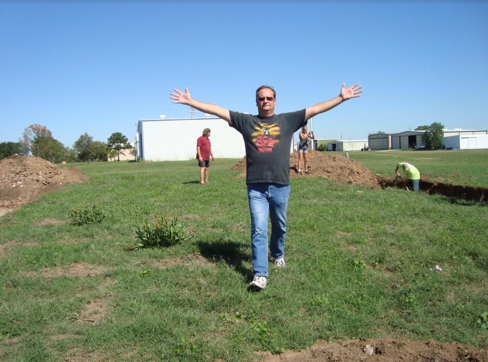 Joe Axline, a man in a field with his arms spread wide.