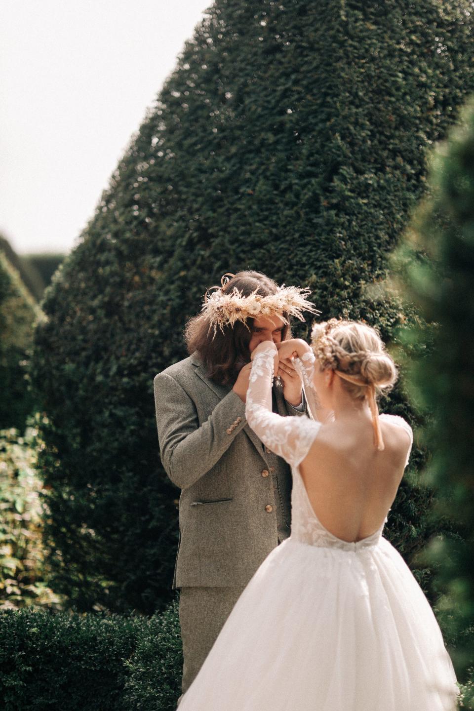 A man kisses his partner's hands in a garden on their wedding day.