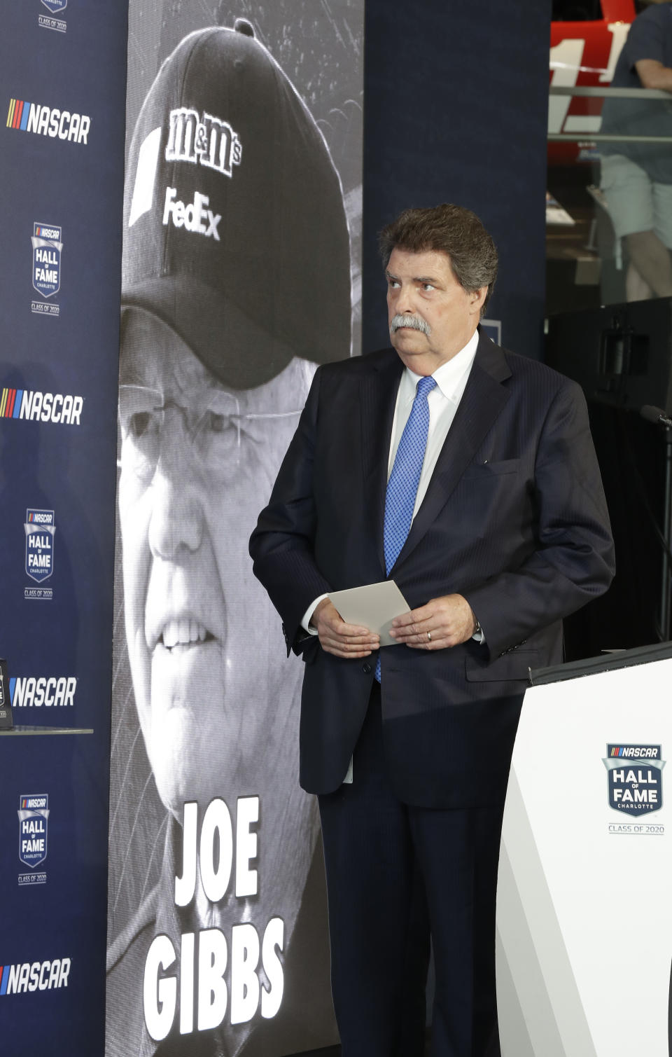 NASCAR vice chairman Mike Helton watches a video after naming team owner Joe Gibbs a member of the NASCAR Hall of Fame, in Charlotte, N.C., Wednesday, May 22, 2019. (AP Photo/Chuck Burton)