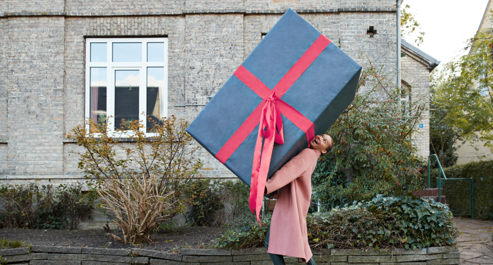 little girl in pink coat walking outside holding giant blue gift box with red ribbon