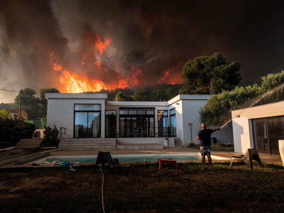 A man uses a garden hose to drench his house before being evacuated as a wild fire burns in the background, in La Couronne, near Marseille: AFP/Getty