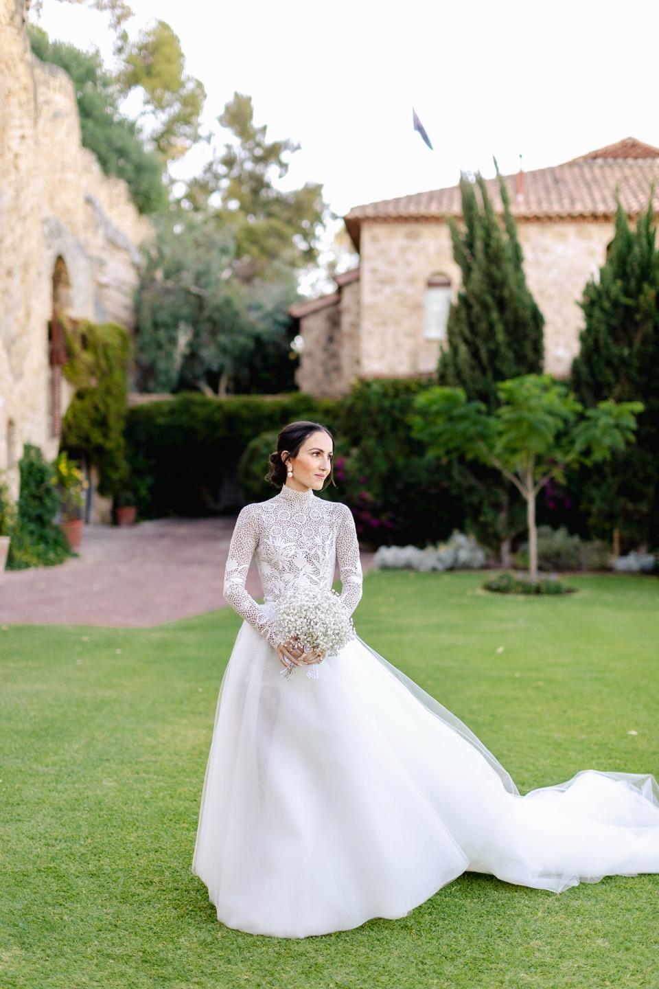 A bride stands in a field in her wedding dress.