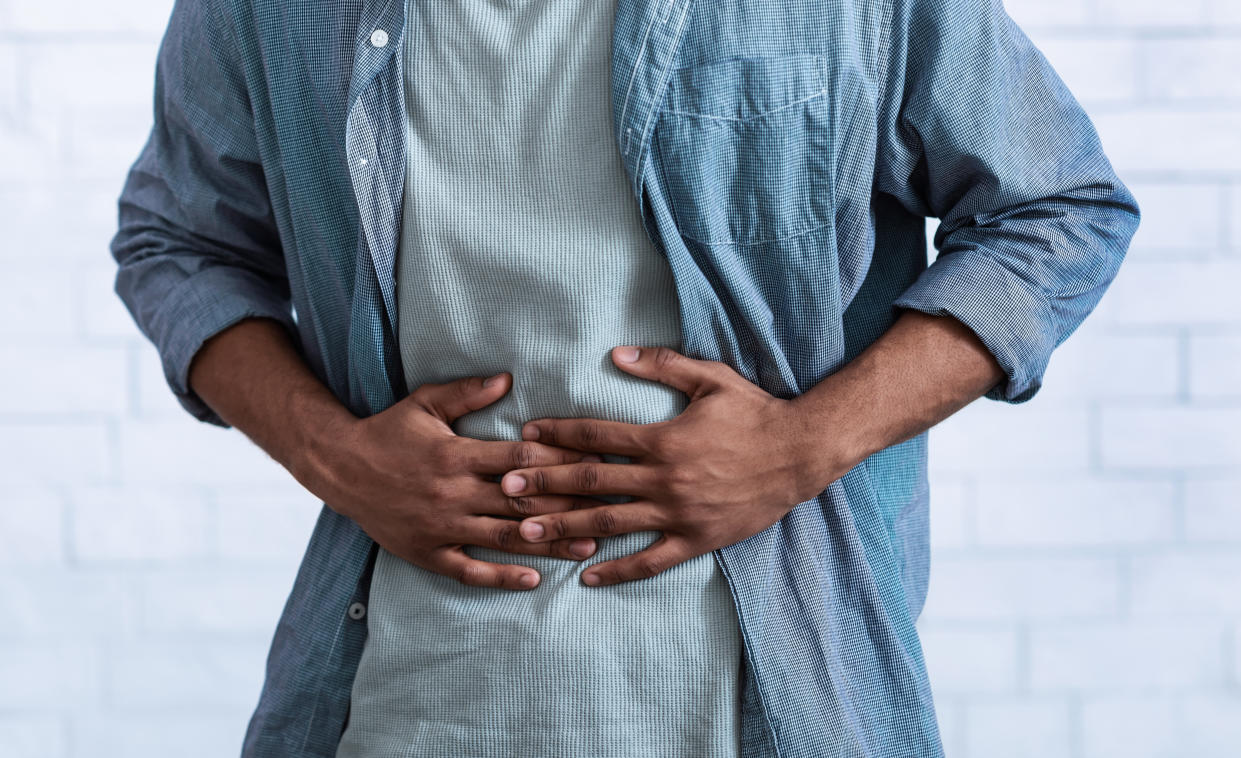 Unrecognizable Black Guy Touching Aching Abdomen Having Painful Stomachache Standing Over Gray Studio Background. African Man Suffering From Stomach Inflammation. Gastritis And Abdomen Pain. Cropped food poisoning