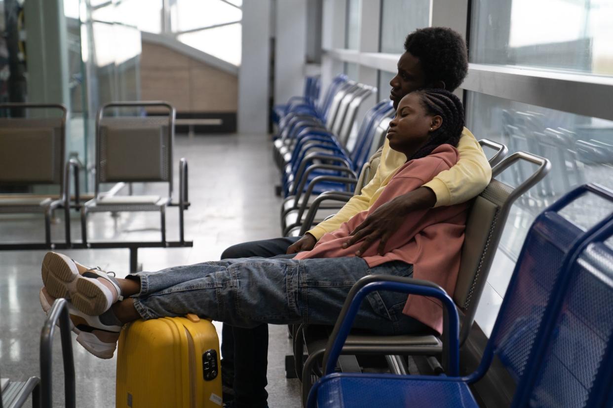 African couple sleeping on chairs in waiting room of airport, tired wait for delayed flight. Black travelers with luggage fly or return from romantic vacation after airlines reopening and covid end