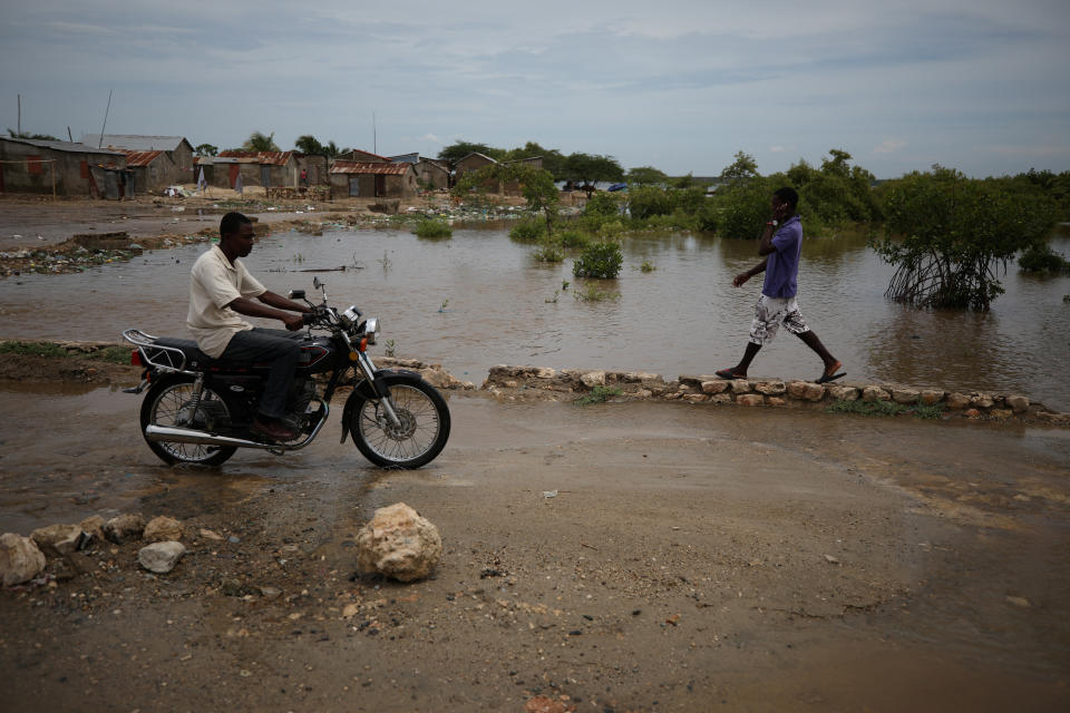 People pass next to a flooded area in Fort Liberte, Haiti