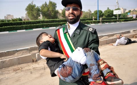 A Revolutionary Guard member carries a wounded boy after a shooting during a military parade in the southwestern city of Ahvaz, Iran. - Credit: AP