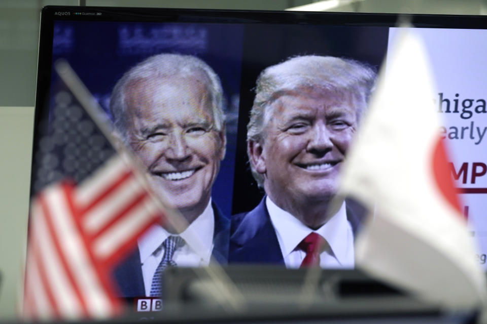 A Japanese and a U.S. flags are placed in front of a TV monitor showing a news program live broadcasting on the U.S. presidential election between President Donald Trump, right, and former Vice President Joe Biden, left, at a foreign exchange dealing company Wednesday, Nov. 4, 2020, in Tokyo. (AP Photo/Eugene Hoshiko)