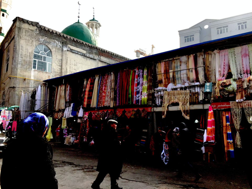 <span class="caption">A fabric market in Urumqi with a mosque in the background, where Uighur women are comfortable covering their heads.</span> <span class="attribution"><span class="source">Sarah Tynen</span></span>