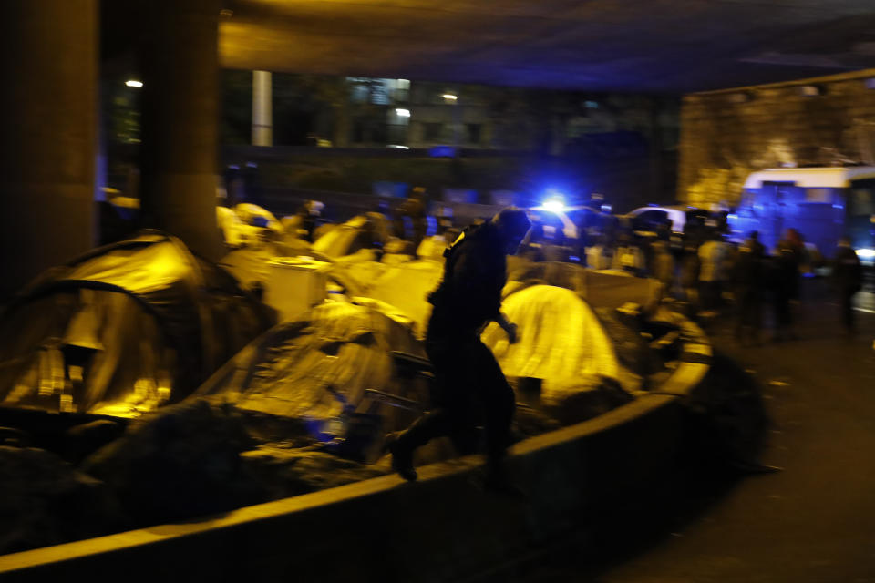 A police officer jumps on the street next to migrants' tents as they clear an area Thursday, Nov. 7, 2019 in the north of Paris. Migrant encampments are becoming increasingly visible in the French capital. Police cleared Thursday several thousand people from a northern Paris neighborhood where migrants have repeatedly been removed. (AP Photo/Francois Mori)