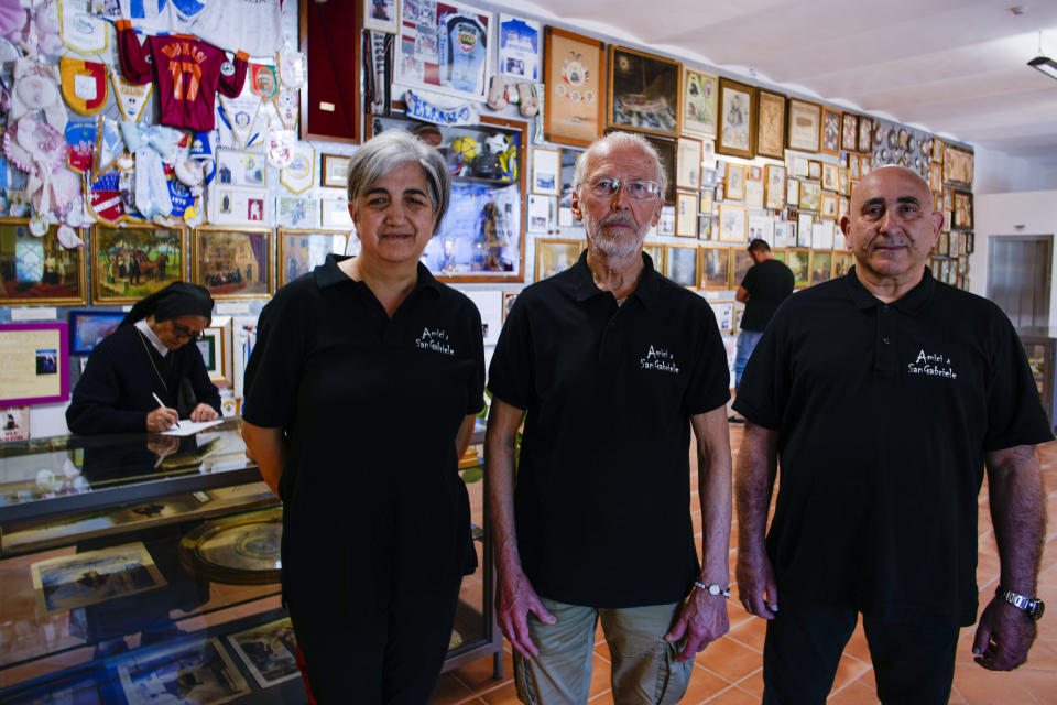 Volunteers of the Amici di San Gabriele (St. Gabriele's Friends) association, from left, Assunta Cantalupo, Roberto Zanella, and Antonino Di Odoardo pose for a portrait inside a room of the St. Gabriele dell'Addolorata sanctuary in Isola del Gran Sasso near Teramo in central Italy, Sunday, June 4, 2023. (AP Photo/Domenico Stinellis)